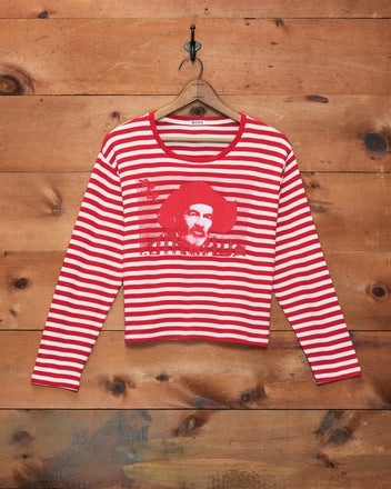 The Rib Stripe Hayes Long Sleeve Tee, with red and white stripes and a printed image of Western-movie sidekick Gabby Hayes, hangs on a wooden wall.