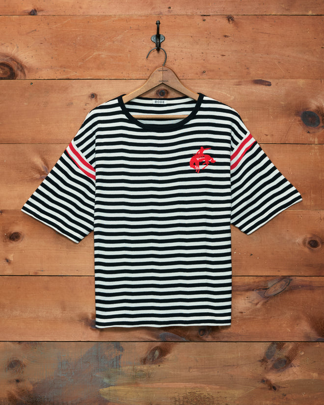 Rib Stripe Training Shirt—a black and white striped ribbed cotton tee featuring red stripes on the sleeves and a red fish graphic on the chest, hanging on a hook.