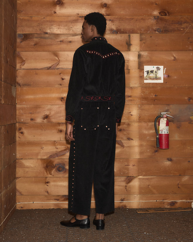 Person wearing a black corduroy Corduroy Copper Spur Jacket and matching trousers with red floral embroidery.