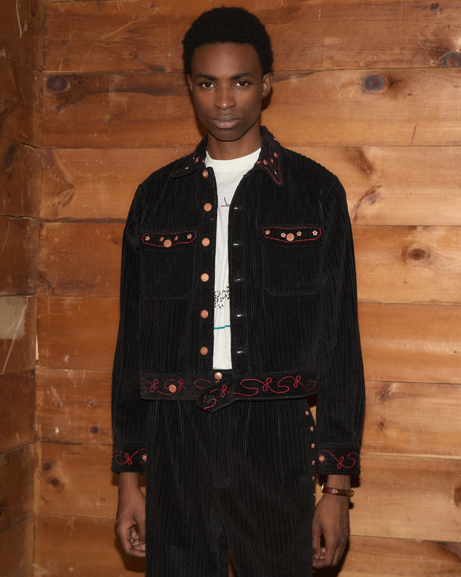 Corduroy Copper Spur Jacket in black wide-wale corduroy with red embroidery and copper buttons in a workwear silhouette.