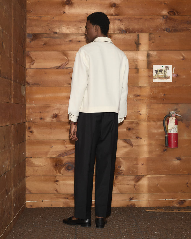 A person seen from behind, wearing an ivory Stockton Jacket with black trim and dark trousers.
