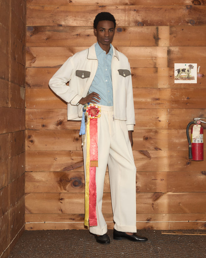 A man in a Stockton Jacket over a light blue shirt and cream trousers with a prize ribbon.