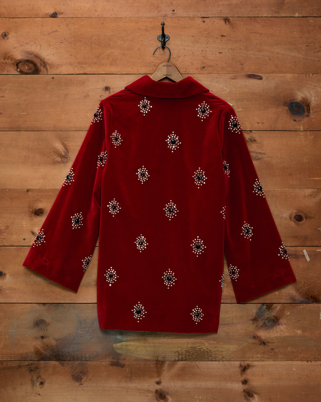 Luminaire Jacket: red velvet swing jacket with long sleeves and scattered beaded embellishments on a wooden wall.