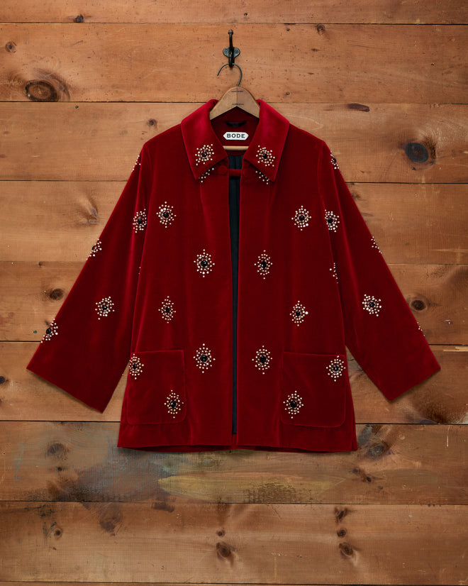 Luminaire Jacket: red velvet swing jacket with an open front and scattered beaded floral embellishments on a wood wall.