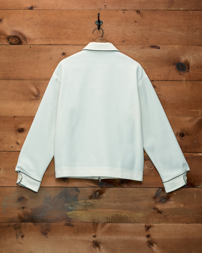 Stockton Jacket: off-white ivory wool children’s cowboy jacket with black trim, hanging on a wood wall.