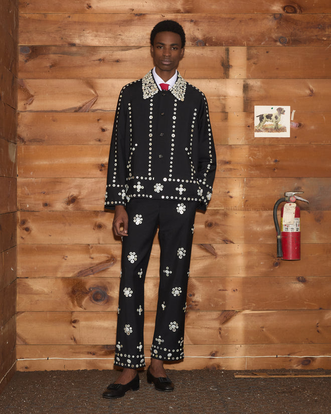 A person in a Pearly Royal Jacket and matching trousers, both featuring white circular floral studs.