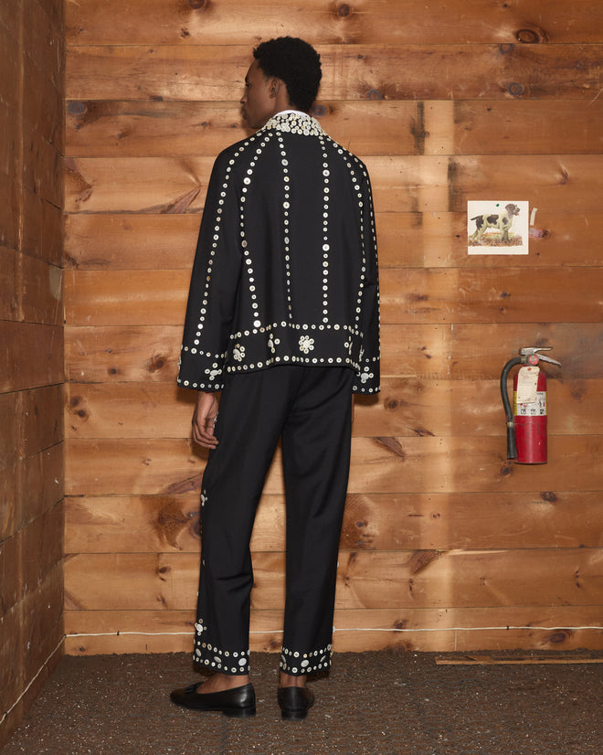 Person viewed from behind wearing a black Pearly Royal Jacket and matching trousers with white circular patterns.