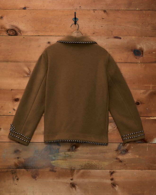 Bradford Smoking Jacket in brown velvet with rope-style trim on the collar and cuffs, hanging on a wooden wall.
