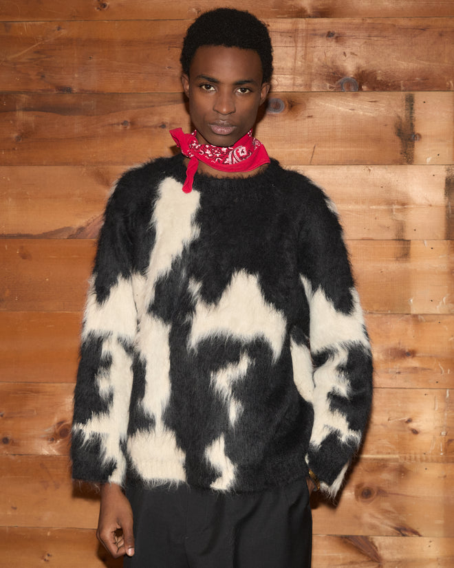 A person wearing the Holstein Sweater - Black/White and a red bandana stands in front of a wooden wall.