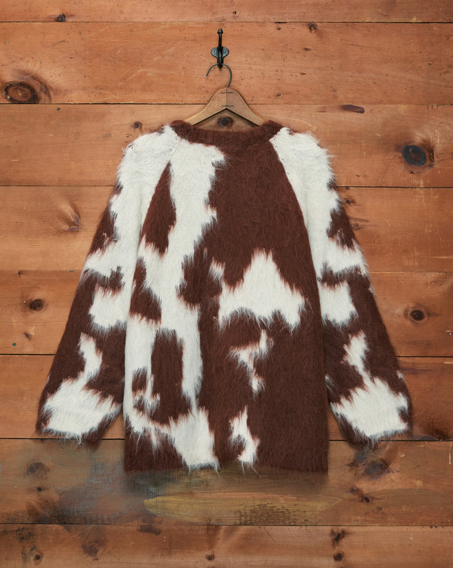 The Holstein Sweater - Brown/White hangs on a wooden wall, displayed on a hanger.