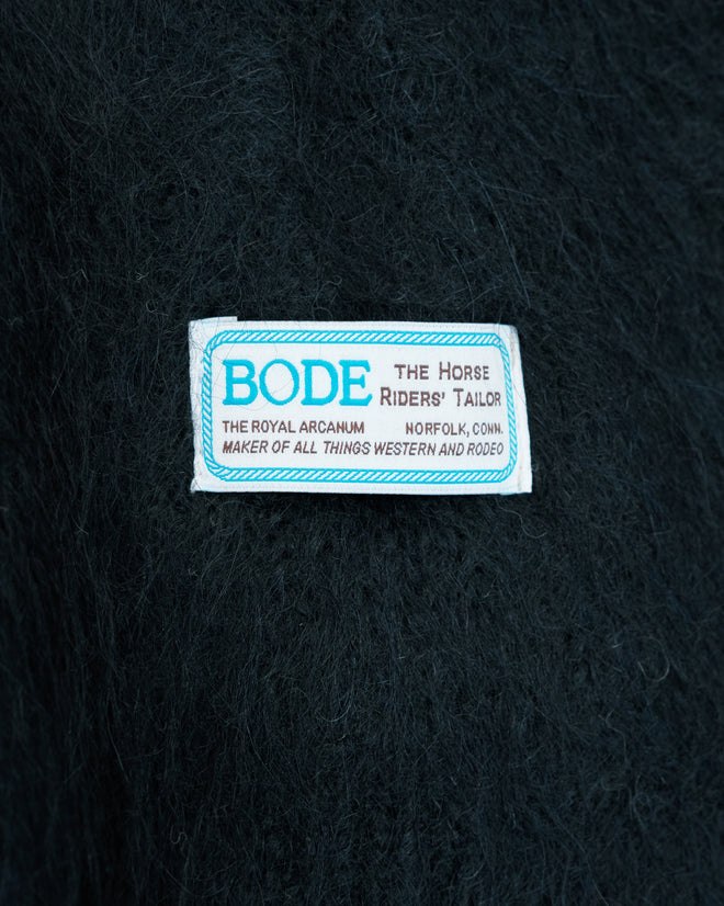 Clothing label reading “BODE The Horse Riders’ Tailor” on a dark fuzzy fabric background, reminiscent of the luxuriously soft brushed alpaca Holstein Sweater in Black/White.