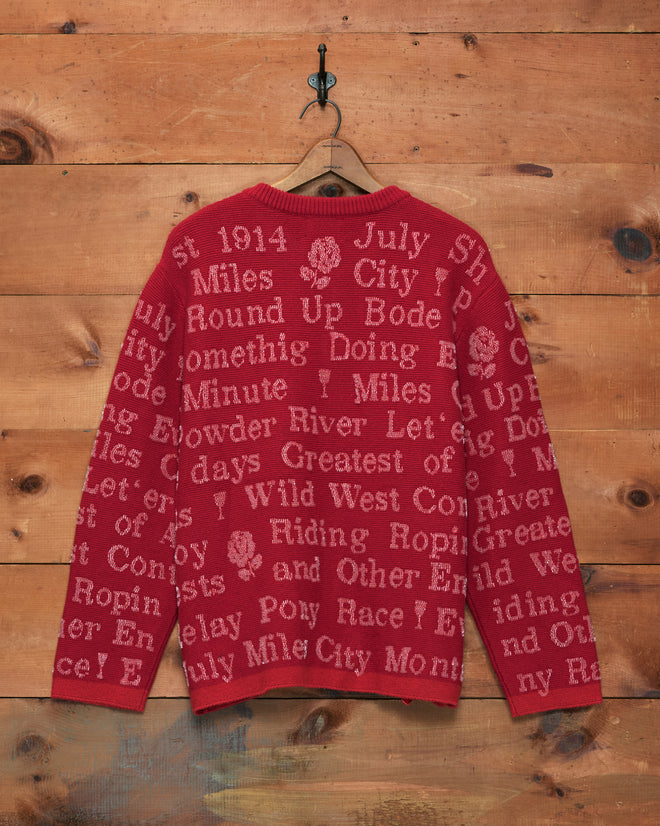 Beaded Round-Up Cardigan featuring a red knit design with various white words and phrases, inspired by classic rodeo cardigans, displayed hanging on a wooden wall.