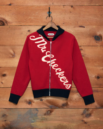 The Mr. Checkers Felted Cardigan features a red design with black collar and cuffs, expertly crafted from 100% wool. “Mr. Checkers” is displayed diagonally across the front, combining classic rodeo knitwear inspiration with a contemporary zip-up cardigan silhouette.