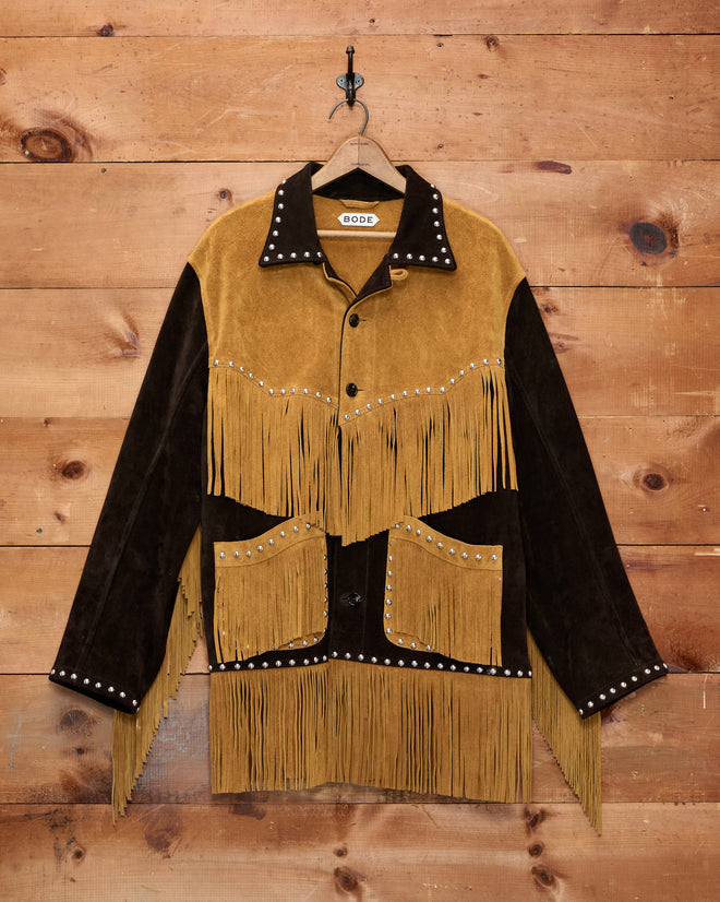 Studded Appalachian Jacket - Brown/Tan: This brown and tan suede fringe cowboy jacket with silver studs hangs on a wooden wall—perfect for a children’s cowboy costume or anyone seeking authentic Western flair.