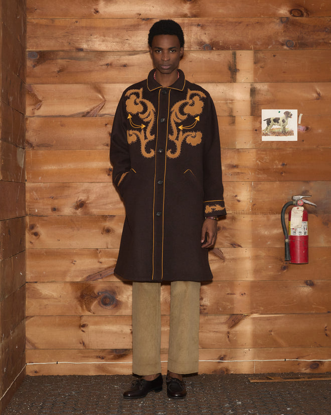 A person wearing a wool Ponderosa Appliqué Coat with yellow floral detail over tan trousers.