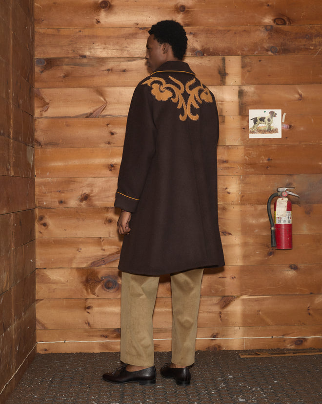 Ponderosa Appliqué Coat: a dark brown wool Western swing coat with orange trim and a floral back appliqué over trousers.