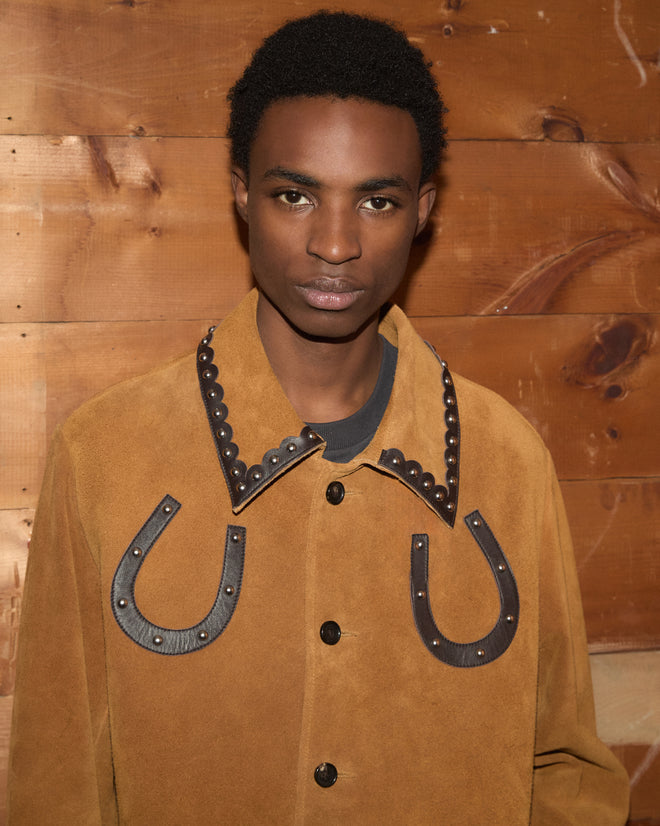 A person wearing the Suede Carson Jacket stands in front of a wooden wall.
