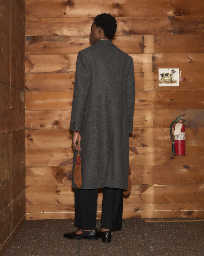 A person viewed from behind wearing a long, dark, double-breasted Buffalo Tweed Coat and black trousers.