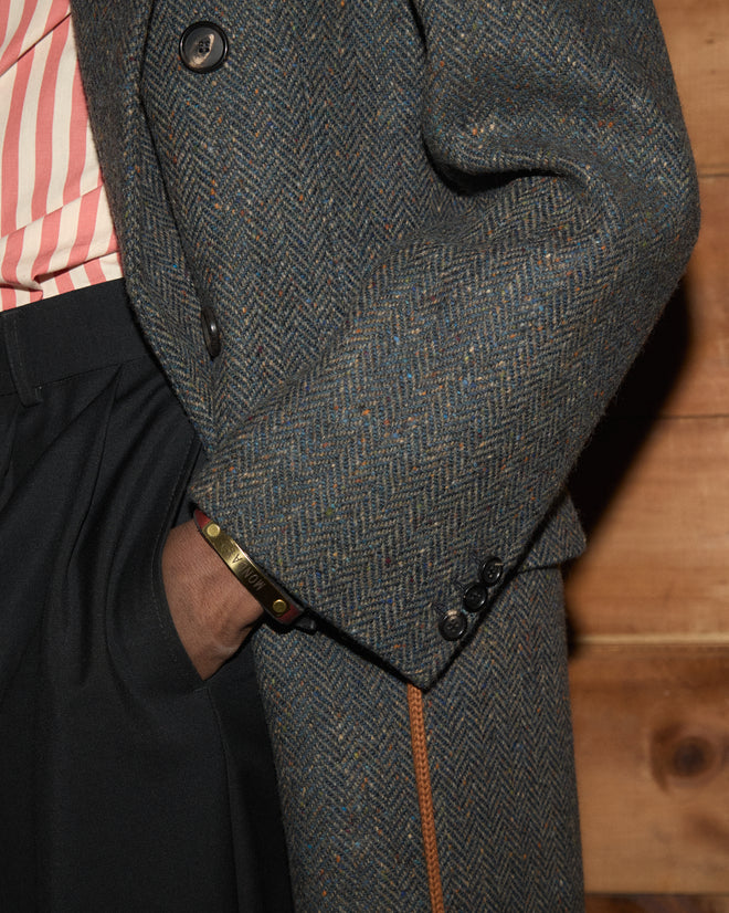 Buffalo Tweed Coat in grey Donegal tweed, worn over dark trousers and a striped shirt.