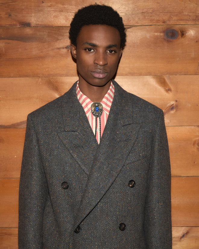 A person wearing a Buffalo Tweed coat, a striped shirt, and a bolo tie.