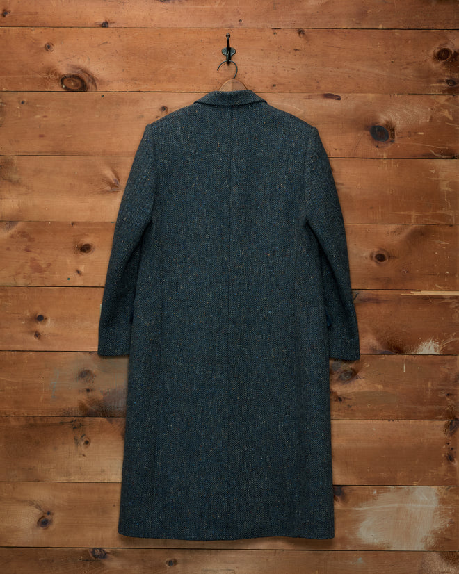 Buffalo Tweed Coat in dark teal herringbone Donegal tweed hanging against a wooden wall.