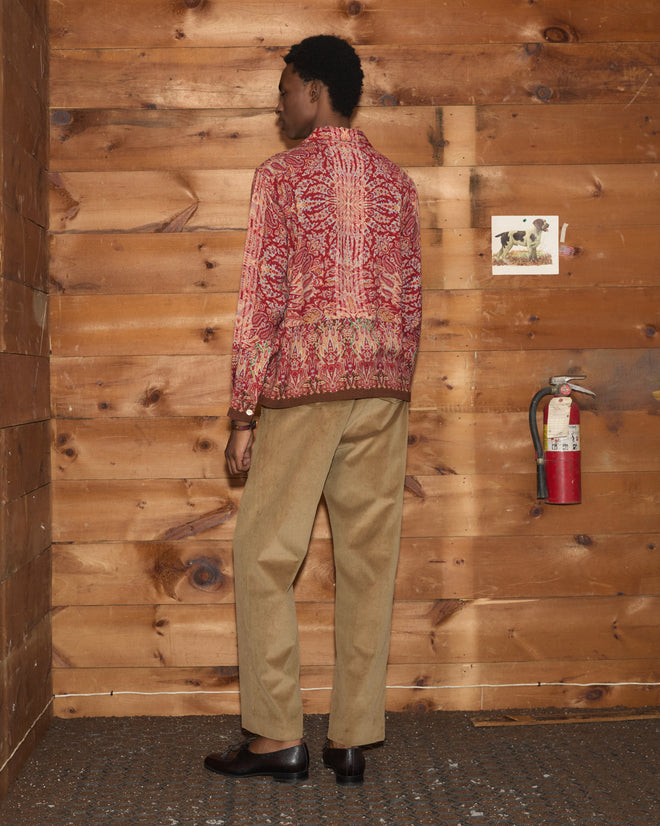 A person wearing the Arrowleaf Long Sleeve Shirt and tan pants stands facing a wooden wall with a fire extinguisher and a small photo.