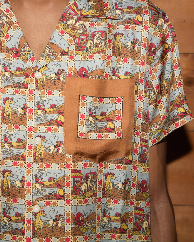 Cowboy Comic Short Sleeve Shirt featuring a chest pocket and cowboy comic print, worn by person; wood wall in background.