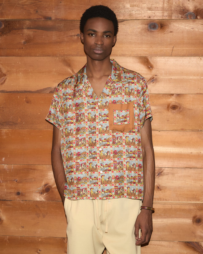 A person wearing the Cowboy Comic Short Sleeve Shirt and light pants stands in front of a wooden wall, facing forward.