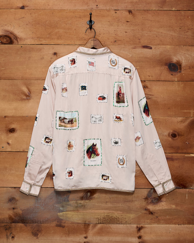 A light pink Equestrian Patch Long Sleeve Shirt, featuring various postage stamp-inspired designs reminiscent of collectible fabric swatches and vintage tobacco silks, hanging on a wooden wall.