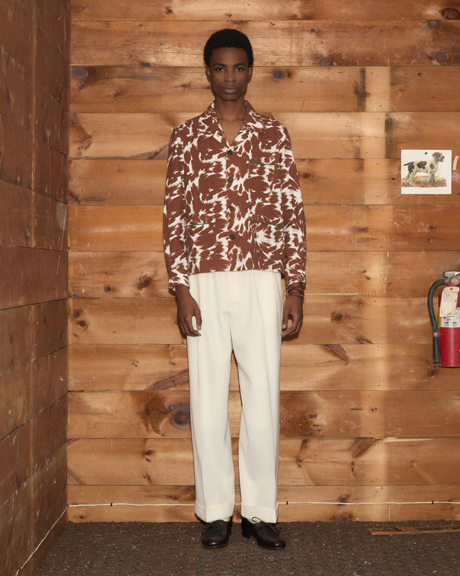 A person in a Flannel Cow Print Long Sleeve Shirt made of 100% cotton and white pants stands indoors against a wooden wall near a fire extinguisher.