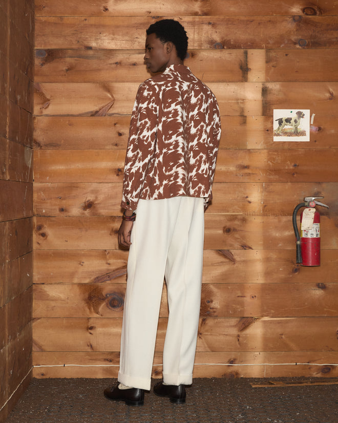 A person stands in a wood-paneled room, wearing white pants and the Flannel Cow Print Long Sleeve Shirt, made from 100% cotton flannel, and faces away.