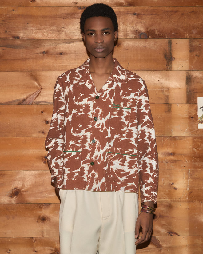A person wearing the Flannel Cow Print Long Sleeve Shirt paired with cream pants stands against a wooden wall.