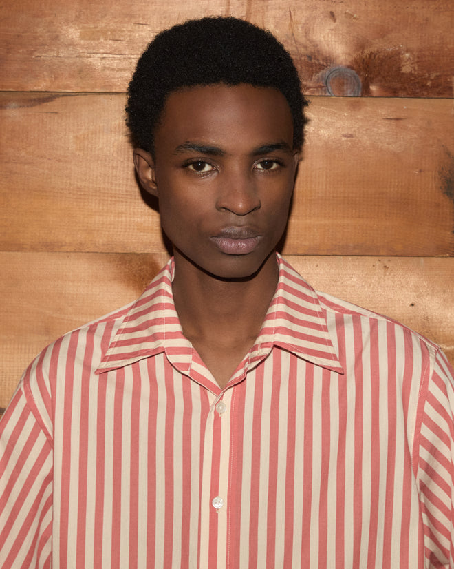 A person wearing the Rancho Long Sleeve Shirt, a vintage striped shirt made in India, stands in front of a wooden wall, looking at the camera.