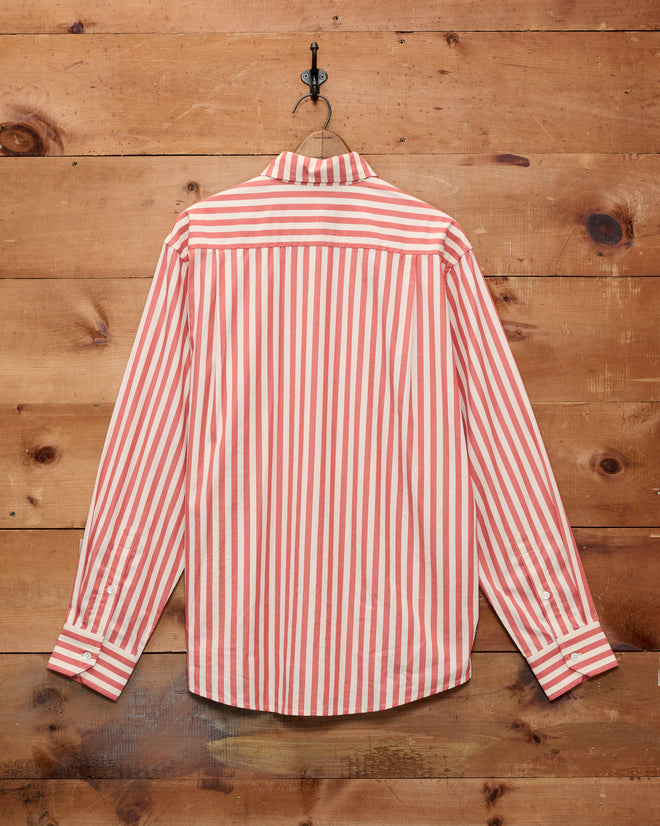 The Rancho Long Sleeve Shirt, crafted in India from 100% cotton, hangs on a hook against a wooden wall; its red and white vertical stripes lend it a timeless, vintage charm.