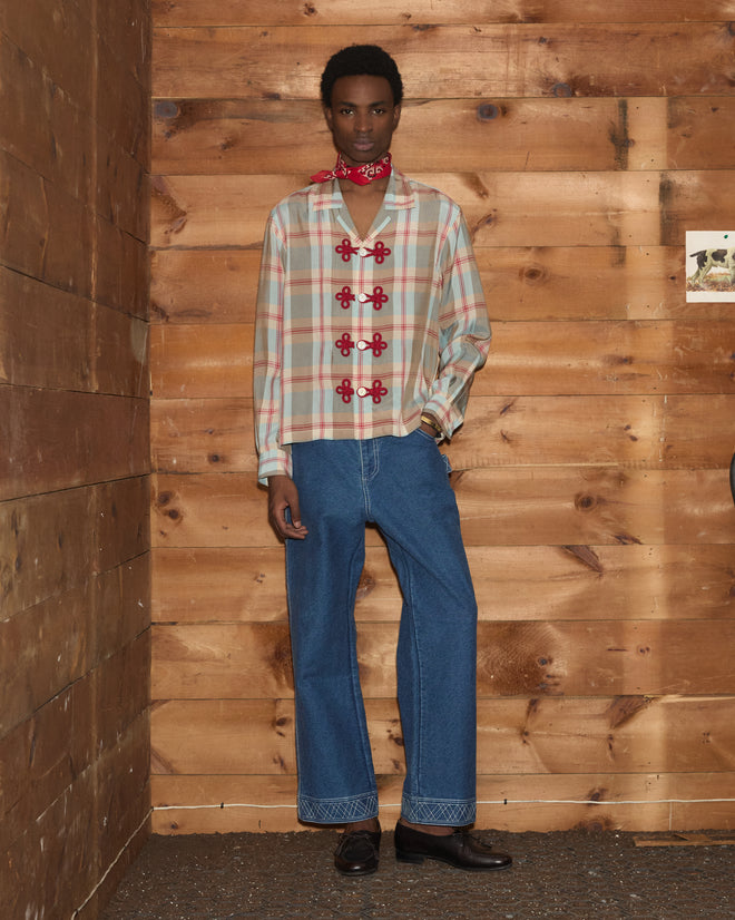 A person wearing the Canyon Trillium Shirt, blue jeans, and a red bandana stands against a wooden wall, looking at the camera.