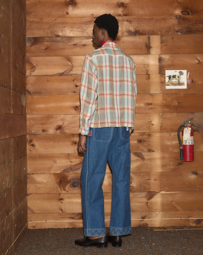 A person wearing the Canyon Trillium Shirt and blue jeans stands facing a wooden wall with a fire extinguisher and a photo.