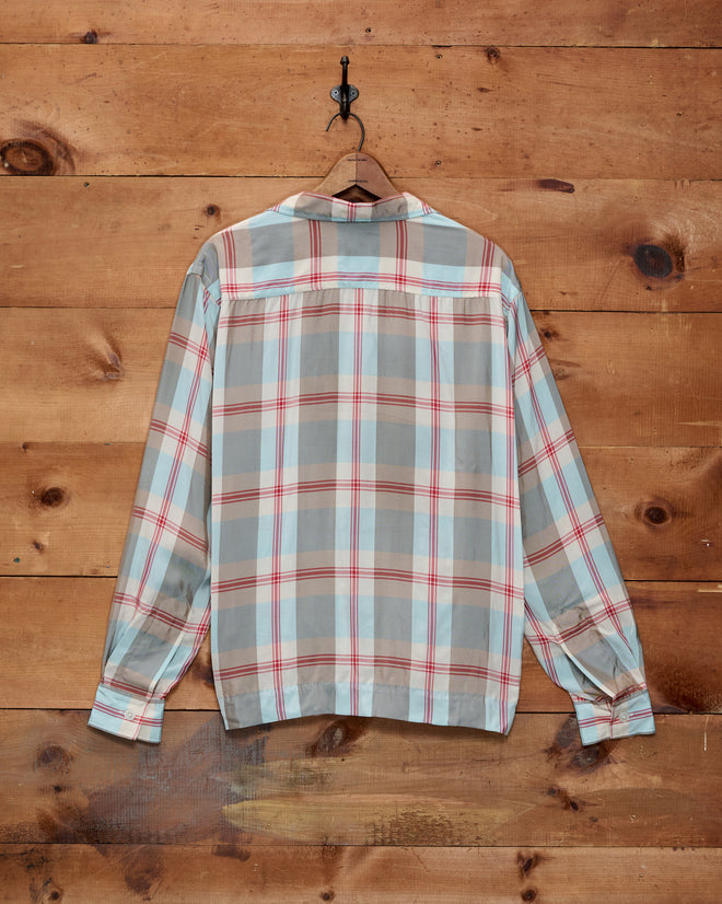 The Canyon Trillium Shirt, a long-sleeve plaid shirt in red and blue with red stripes, hangs on a hook against a wooden wall.