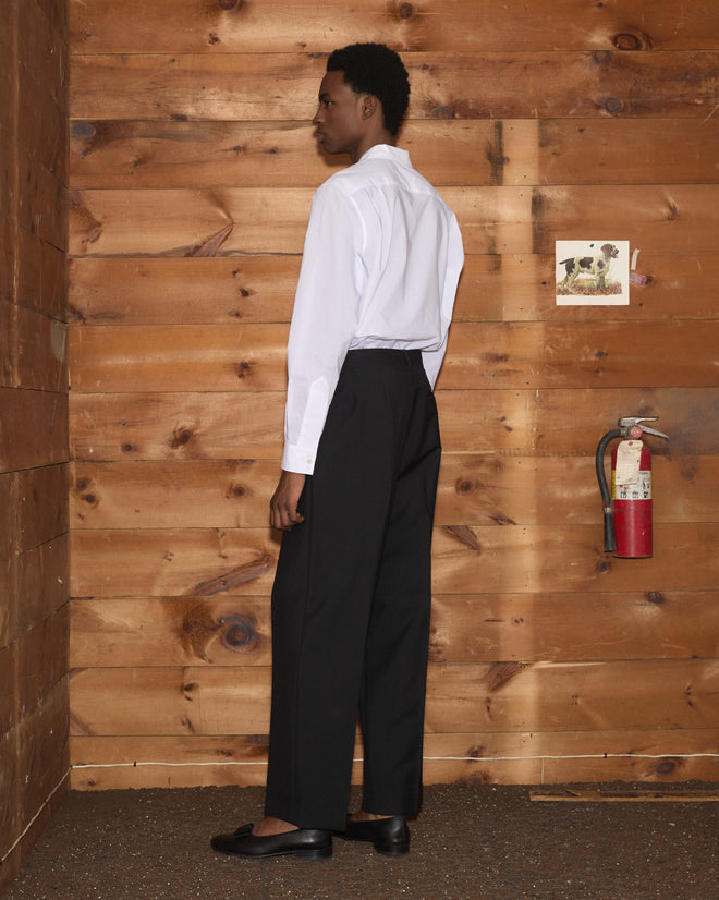A person seen from behind wears a white Clover Charm Long Sleeve Shirt and black trousers.