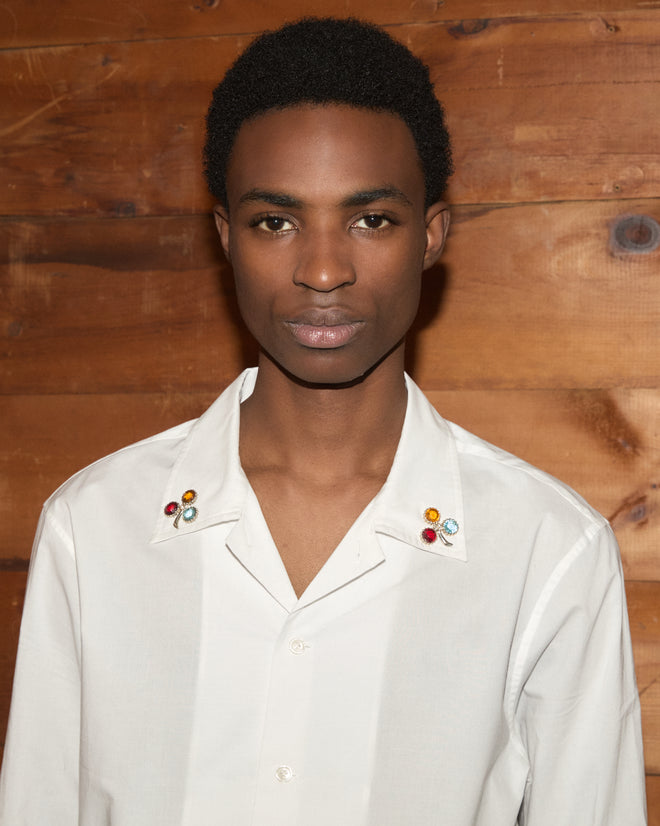 A person wearing a white cotton poplin Clover Charm Long Sleeve Shirt with gemstone clover charms on the collar.