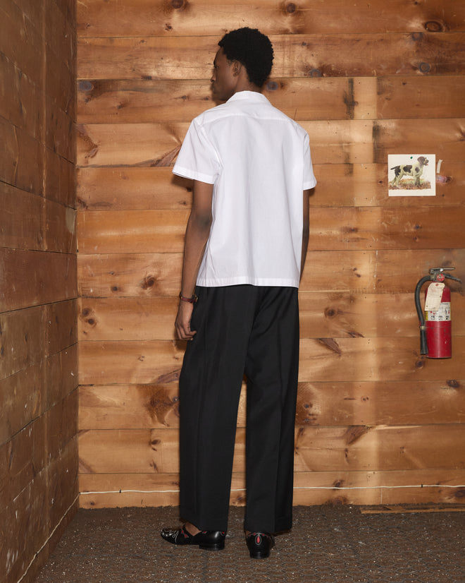 A person seen from behind wears a white Clover Charm Short Sleeve Shirt and black trousers.