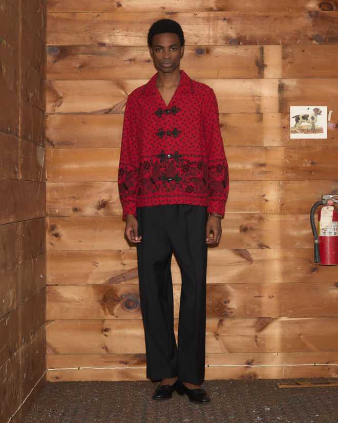 A person wearing the Beaded Kerchief Long Sleeve Shirt and black pants stands against wooden walls near a fire extinguisher.