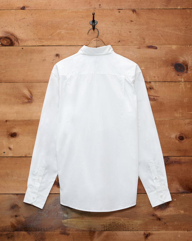 The Button Jar Tuxedo Shirt, shown from the back as it hangs on a hook against a wooden wall, is crafted from 100% cotton and features a classic pleated bib design.