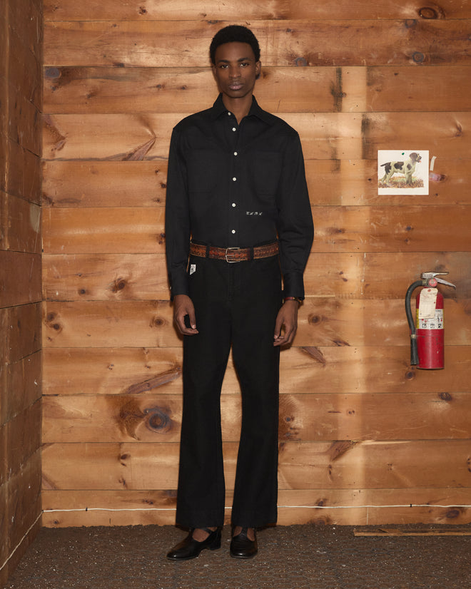 Wearing the Faille Western Shirt, a person stands in a wooden room with a fire extinguisher and a small animal photo on the wall.