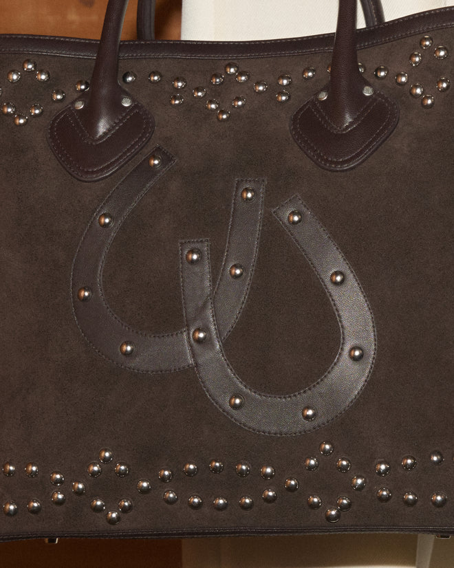 Studded Horseshoe Tote crafted from brown cow suede, featuring silver studs and an overlapping leather horseshoe appliqué on the front.