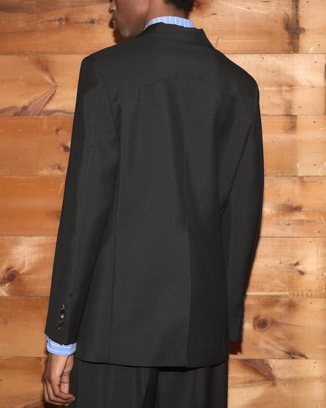A person wears a black Mohair Western Suit Jacket over a blue striped shirt.