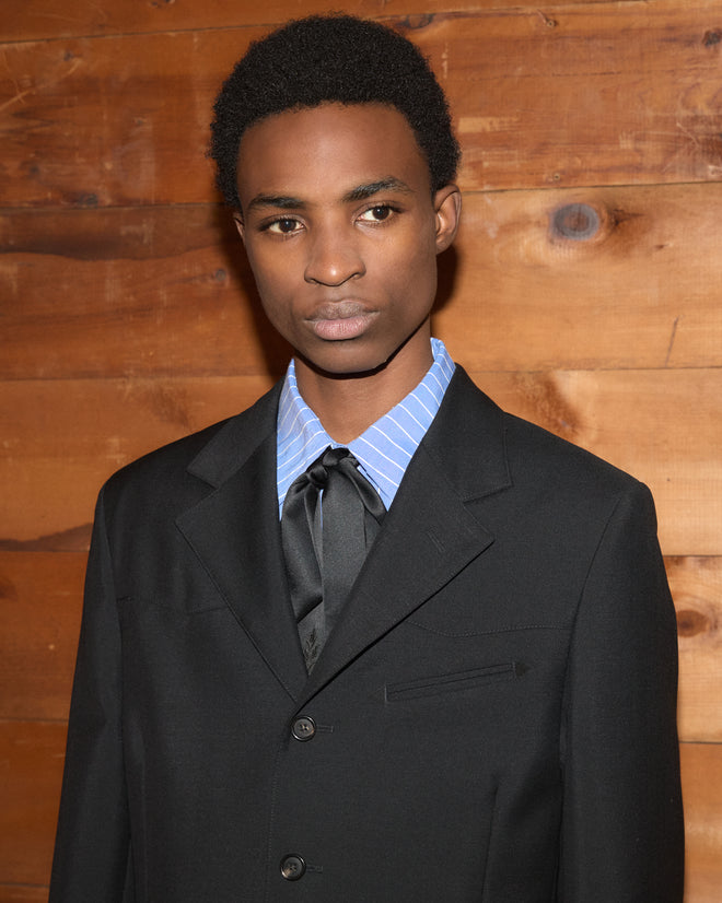 A person wears a wool Mohair Western Suit Jacket over a blue striped shirt with a black necktie.