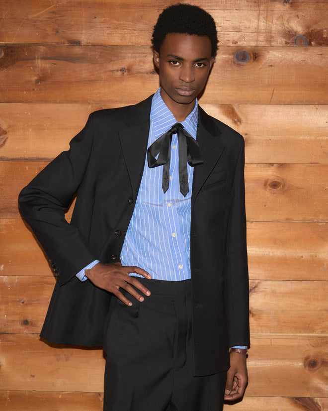 A person wearing a Mohair Western Suit Jacket over a blue striped button-down shirt with a black necktie.