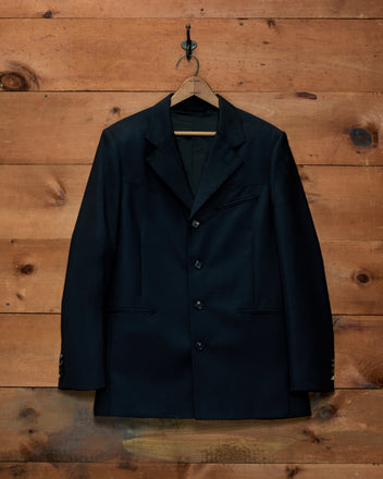 A dark wool Mohair Western Suit Jacket on a wooden hanger against a wood-paneled wall.
