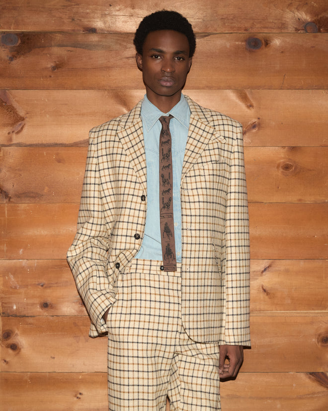 A man in a Sandhill Plaid Hacking Jacket and matching trousers over a blue button-down shirt and brown patterned tie.