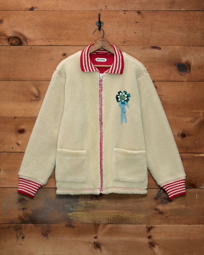 Woolly Warmup Jacket: cream-colored sherpa cardigan with a striped collar, cuffs, and a horse ribbon pin.